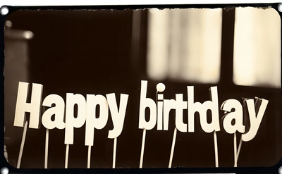 A happy Birthday sign is displayed on a table top with candles in the background and a black and white photo of a piano in the background, post processed, a pastel, international typographic style